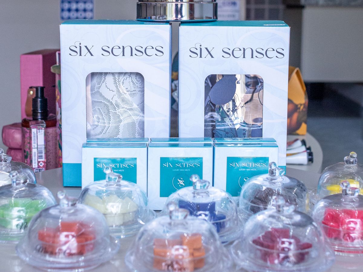 Kits Six Senses com aromatizador e ceras perfumadas coloridas sob redomas, na mesa central da Astre
